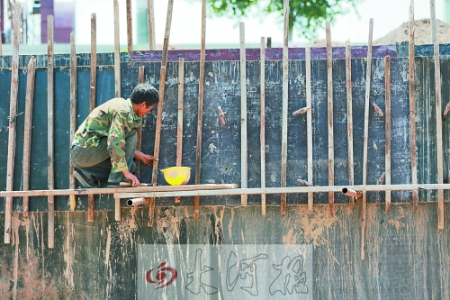 　　烈日下，狹窄的架子上，工人正用錘子固定樁基。