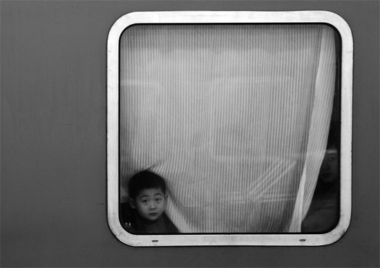 一個孩子把頭伸向窗外，他想再看送別的親人一眼