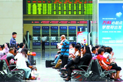 候車大廳溫度很高，一名乘客一手扇風(fēng)、一手擦汗