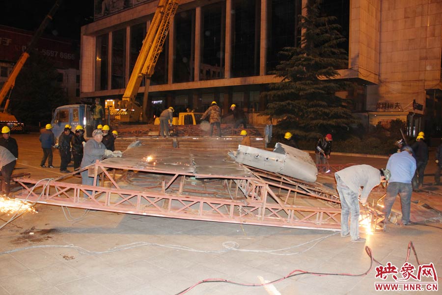 地面上的20多名工人對(duì)吊裝下的廣告牌進(jìn)行分割。