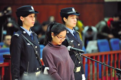 被告人盧梅低著頭，站在朝陽法院刑事審判庭的被告席上。