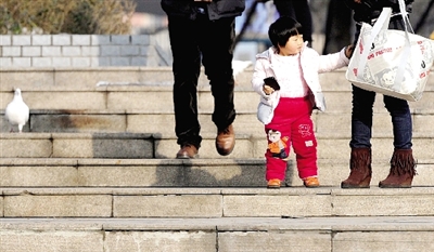 昨天中午，一女孩拉著家長(zhǎng)的手在紫荊山公園曬太陽，氣溫升高，孩子的棉衣解開了扣子。