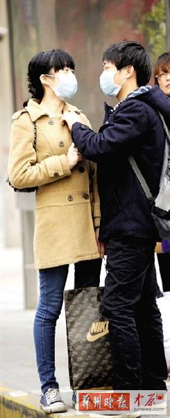 公交站臺(tái)上，一對(duì)年輕人戴著口罩，系緊衣領(lǐng)。